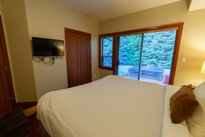 Un dormitorio con una cama grande, un televisor montado en la pared y una ventana con persianas.
