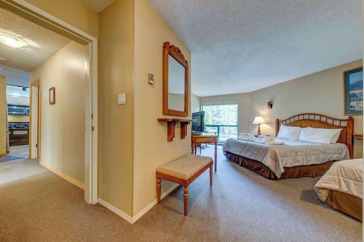 A hotel room with a bed, a bench, a mirror, a TV, and a window.