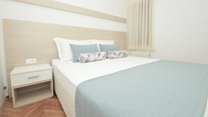 Un lit bien fait, recouvert d’une couverture bleu clair, avec une tête de lit en bois et deux coussins à motifs floraux.