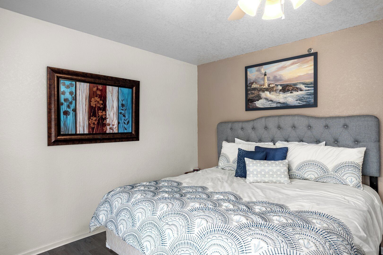 Une chambre à coucher avec une tête de lit capitonnée, une couvre-lit à motifs et deux œuvres d’art encadrées accrochées aux murs.