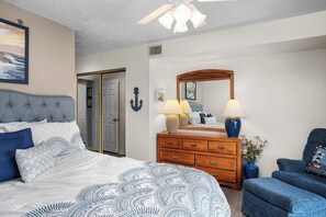 A bedroom with a bed, dresser, chair, and a ceiling fan.