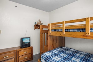 A bunk bed with a wooden frame, a television on a dresser, and a plaid bedspread.