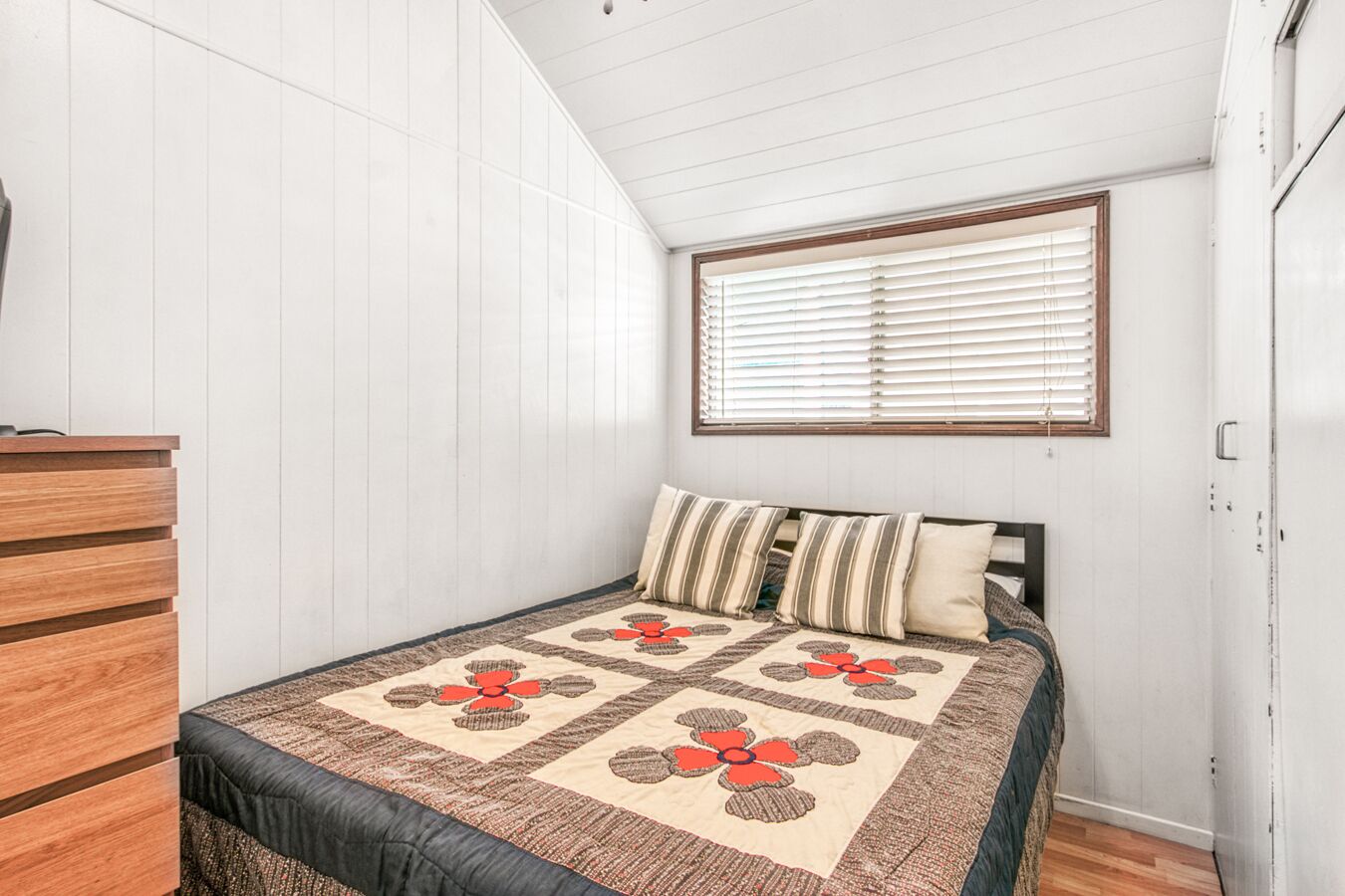 A bedroom with a bed, a wooden dresser, and a window with blinds.