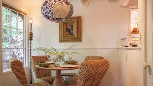 Een eetgedeelte met een ronde tafel, rieten stoelen, een vaas met bloemen en een hanglamp.