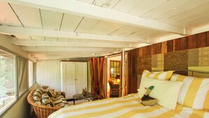 Een kamer met een bed, een rieten stoel, een tafeltje en een deur naar een andere kamer.