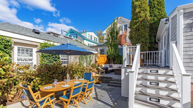 Eine Terrasse mit Holztisch und -stühlen, einem blauen Sonnenschirm und einer Treppe zu einer Außenterrasse.