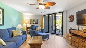 A living room with a blue sofa, a wooden coffee table, a blue armchair, and a ceiling fan.