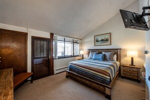Une chambre à coucher avec un grand lit, un banc en bois, une fenêtre et un téléviseur fixé au mur.