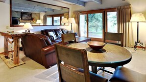 Un salon chaleureux avec un canapé en cuir marron, une table à manger en bois et ses chaises, un grand miroir et une cheminée en pierre.