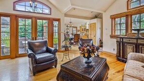 A spacious living room with a leather sofa, a coffee table with a vase, and large windows offering a view of the outdoors. - La Vita Dolce – Romantic Carmel-by-the-Sea Cottage Near Beach & Ocean Ave (Carmel by the Sea)