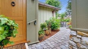 A wooden front door, a small outdoor seating area, and a stone wall. - La Vita Dolce – Romantic Carmel-by-the-Sea Cottage Near Beach & Ocean Ave (Carmel by the Sea)
