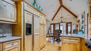 A spacious kitchen with wooden cabinets, a marble countertop, and a dining area with a chandelier. - La Vita Dolce – Romantic Carmel-by-the-Sea Cottage Near Beach & Ocean Ave (Carmel by the Sea)