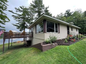 A house with a deck, a small garden, and a view of a lake.