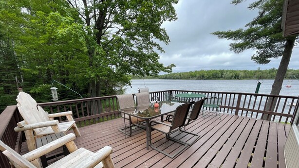 A wooden deck with Adirondack chairs, a table, and a view of a lake.