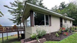A house with a deck, large windows, and a garden with flowers and plants.