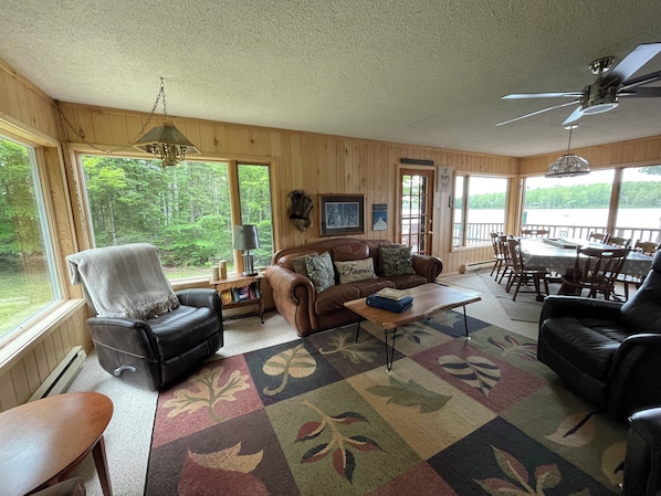 A cozy cabin interior with a leather sofa, a coffee table, and a dining area with wooden chairs.