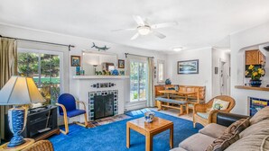 Ein Wohnzimmer mit Kamin, blauem Teppich und Deckenventilator.