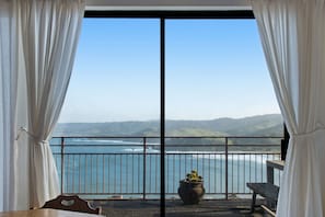 Enjoy breathtaking views of the coastal landscape from this room's spacious balcony, featuring a seating area with a bench and table.