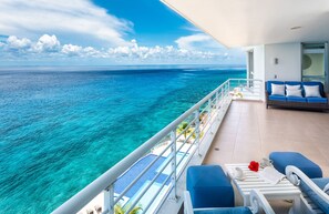 Un balcone con vista sull'oceano, un divano, un tavolo con un fiore rosso e una ringhiera bianca.