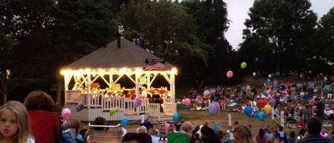 A gazebo with a stage and American flag, surrounded by a crowd of people and colorful balloons.