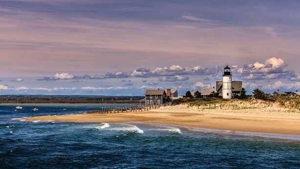 A coastal scene with a lighthouse, beach, and ocean.