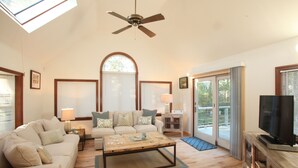 A spacious living room with a ceiling fan, a large arched window, a television, and a sliding glass door leading to an outdoor area.