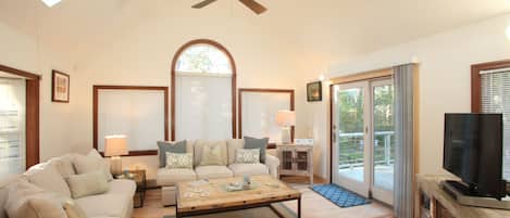 A spacious living room with a ceiling fan, a large arched window, a television, and a sliding glass door leading to an outdoor area.