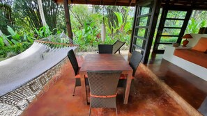 Une table en bois, des chaises en osier, un hamac et une vue sur une végétation luxuriante.