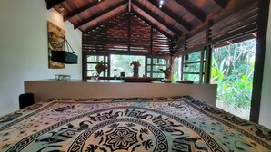 A room with a large bed, a window with a view of greenery, a hanging plant, and a wooden ceiling. - Stylish Open Living, Garden Bathroom & Pool for Honeymooner and Nature Lovers (Uvita)