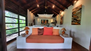 A spacious bedroom with a large bed, two bedside lamps, and a view of the outdoors through large windows. - Stylish Open Living, Garden Bathroom & Pool for Honeymooner and Nature Lovers (Uvita)