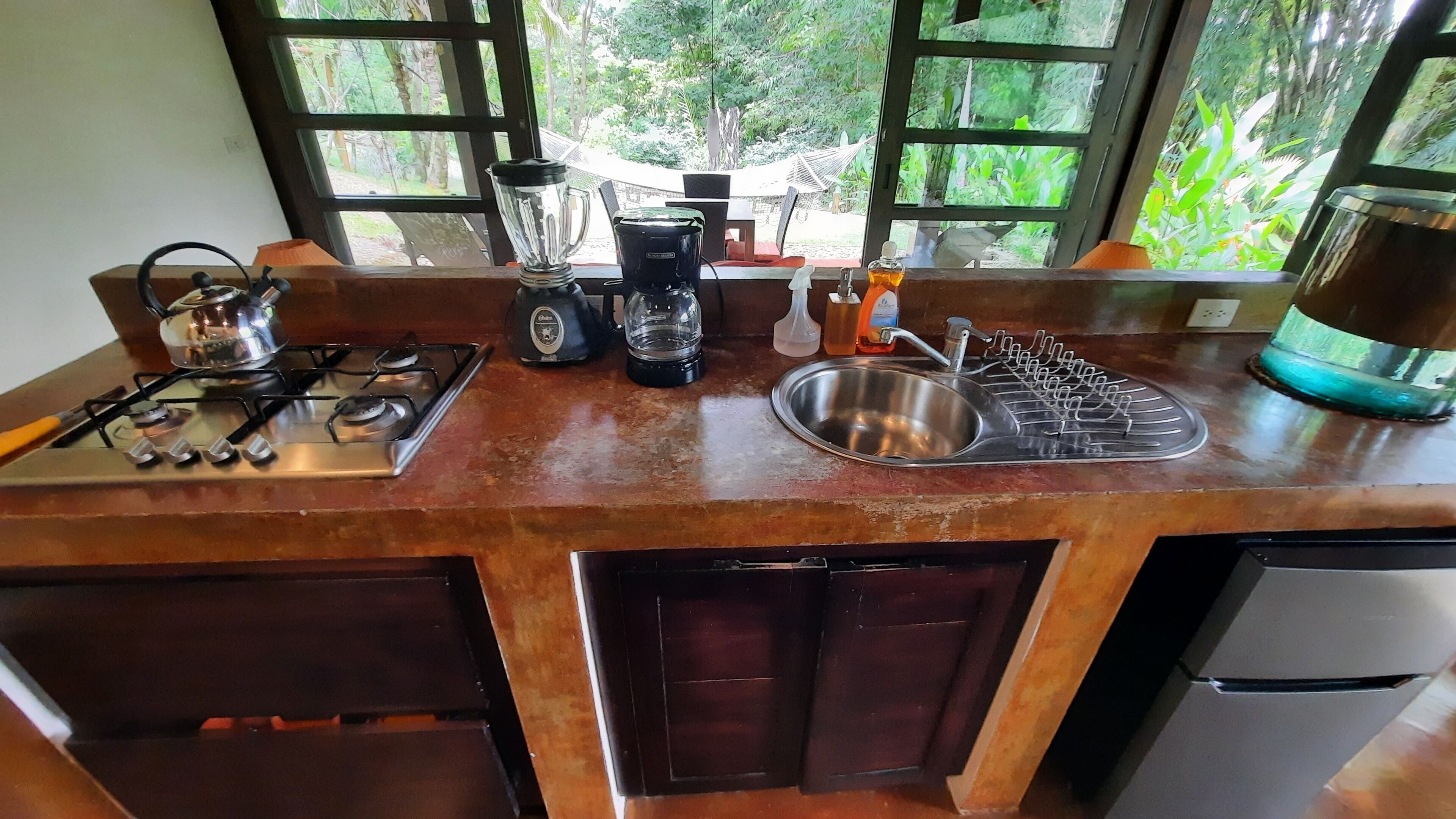 Una cocina con estufa a gas, licuadora, cafetera, pileta con grifo y refrigerador.