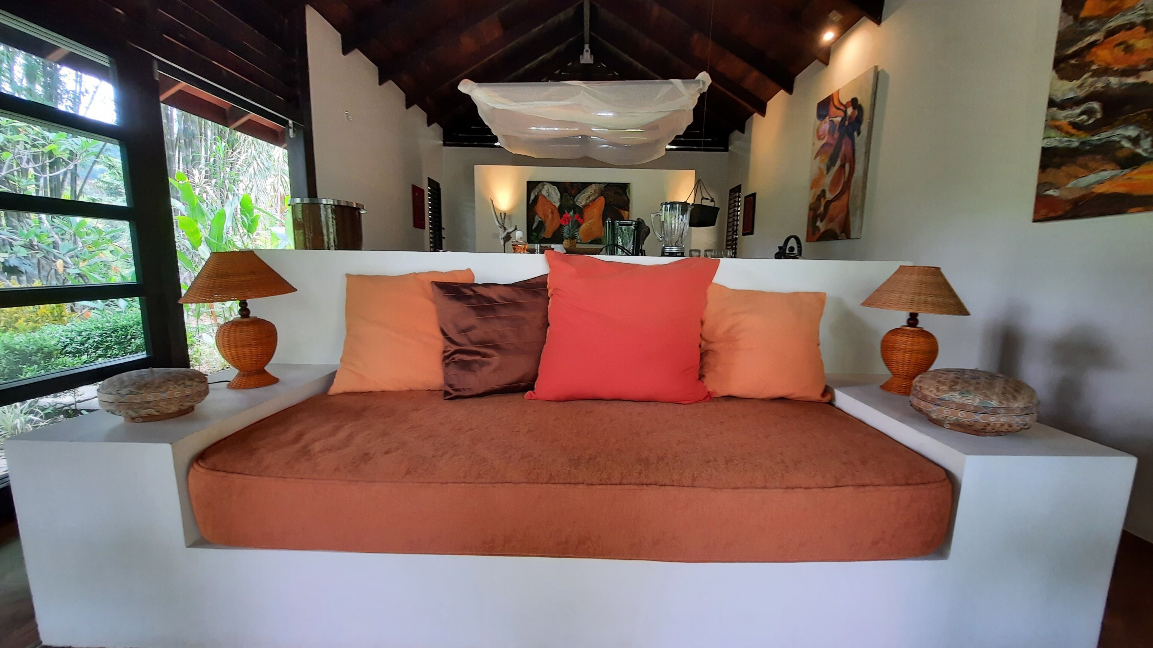 Una cama con una colcha marrón y varias almohadas, con dos lámparas de mimbre a cada lado.