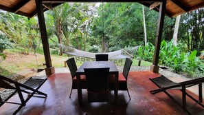 Un espace extérieur abrité, aménagé pour prendre les repas, avec une table et des chaises, entouré d’une végétation luxuriante et agrémenté d’un hamac.