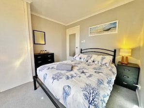 Ein Schlafzimmer mit einem Bett, einem Nachttisch, einer Kommode, einer Tür und einem an der Wand hängenden Bild.