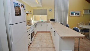 Una cuina compacta amb armaris blancs, un frigorífic, microones i menjador amb cadires i taula.