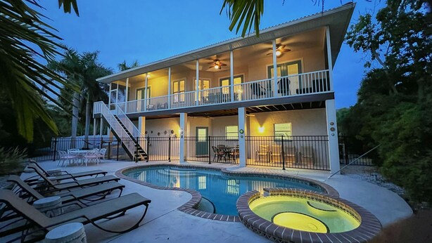 A two-story house with a swimming pool, outdoor furniture, and a balcony. - Canal front pool home on the north end of Anna Maria Island (Anna Maria)