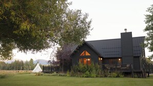Eine Blockhütte mit großer Veranda, Schornstein und einem Zelt im Hintergrund.