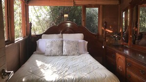 A wooden-framed bedroom with a large bed, multiple pillows, a dresser, and a mirror.