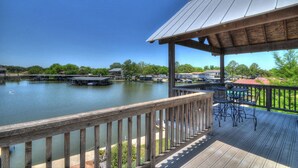 A wooden deck with a metal roof overlooking a calm lake with boats, surrounded by greenery and buildings. - Monthly rental getaway on lake LBJ (Kingsland)