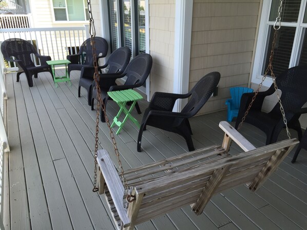 A porch with wicker chairs, a swing, and a small table.
