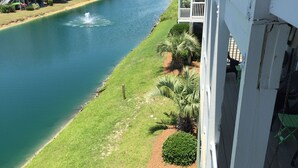 A river with a fountain, surrounded by a grassy area with palm trees and a row of white buildings with balconies. -  Beautiful 4 BR Oib Condo with Beachfront Pool!  (Ocean Isle Beach)