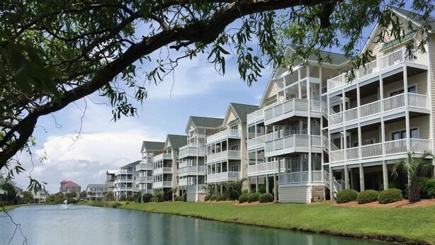 A waterfront hotel with multiple balconies, a calm lake, and a clear sky. -  Beautiful 4 BR Oib Condo with Beachfront Pool!  (Ocean Isle Beach)