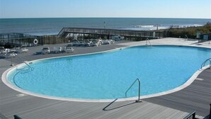 A pool with a wooden deck, lounge chairs, and a view of the ocean. -  Beautiful 4 BR Oib Condo with Beachfront Pool!  (Ocean Isle Beach)