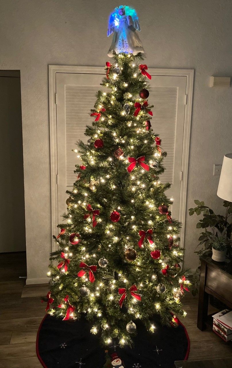 Un albero di Natale decorato con luci e ornamenti, posizionato in una stanza con una porta e una lampada sullo sfondo.