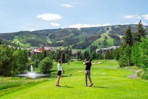 Un parcours de golf avec un étang, des arbres et une chaîne de montagnes en arrière-plan.