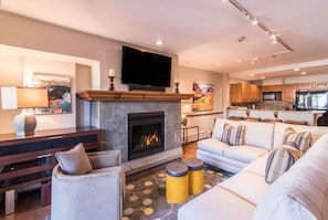 A modern living room with a fireplace, a flat-screen TV, a sofa, and a dining area with wooden cabinets.