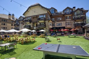 An outdoor seating area with tables and chairs, a ping pong table, and a building with multiple balconies and windows.