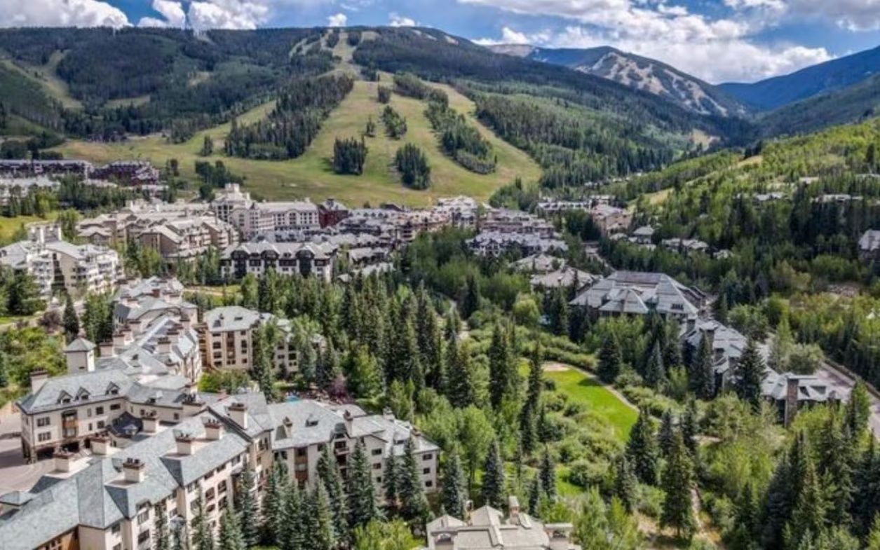 Zona turística de muntanya amb diversos edificis, probablement hotels, envoltada per boscos densos i turons.