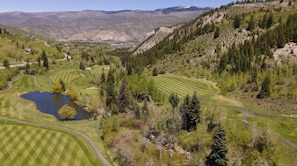 A golf course with a pond, surrounded by trees and hills.