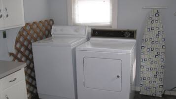 Une buanderie équipée de deux machines à laver et de deux sèche-linge superposés, d’un mur en treillis de bois, d’une fenêtre avec des stores et d’un rideau de douche à motifs.
